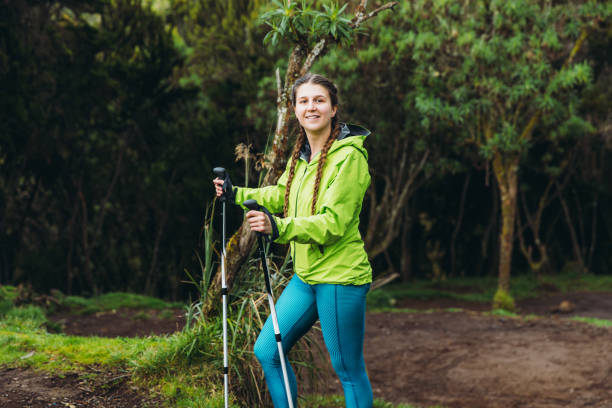 Happy smiling woman with long hair and in green jacket hiking to the top of Kilimanjaro thought the beautiful green forest in Tanzania